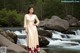 A woman in a long dress standing on a rock by a river.